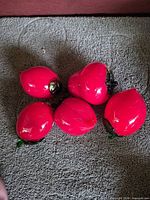Five red glass fruits with green accents grouped on surface