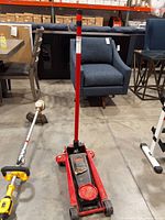 Full view of red hydraulic floor jack with handle upright
