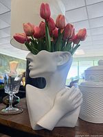 Front left view of white ceramic abstract bust vase with artificial pink tulips