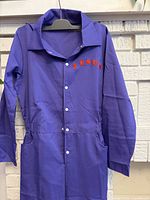 Front view of purple jumpsuit hanging, showing snap buttons and pockets