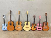 Front view of seven guitars lined up showing variety of finishes and sizes