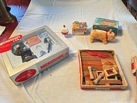 Group shot of all four items on table: boxed microscope set, Wiz-zzer top and box, wind-up pig and box, tray of wooden blocks