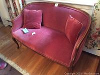 Vintage rose loveseat with two matching pillows on wooden floor near window.