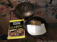 10 inch cast iron frying pan, Lodge cast iron covered Dutch oven, and Cast Iron Cooking For Dummies cookbook displayed on floor.