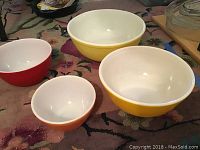 Four vintage Pyrex mixing bowls in red, orange, yellow, and pale yellow, shown from a side angle.
