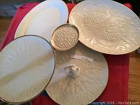 Five serving plates and platters on red cloth, showing embossed designs and shapes.