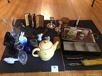 Wide shot of the assorted items including tea pot, candle sticks, vases, trays, small figurines, and boxes on black background