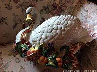 Side view of white ceramic swan planter with colorful painted fruit and leaves, showing detailed feathers and gold beak