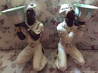 Front view of both ceramic statues on floral upholstery, showing details, colors, and posture