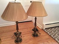 Two brass Stiffel lamps side by side with pleated shades on hardwood floor.