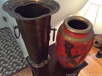 Two umbrella stands on a table, showing the tall dark metal and the red ceramic one