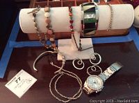 Various bracelets, necklaces, earrings and a Fossil wristwatch displayed on a table and bracelet holder.