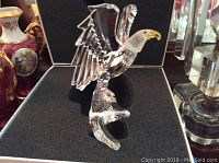 Crystal eagle figurine with clear faceted wings, yellow beak, mounted on textured crystal base inside fitted black foam in hinged display box.