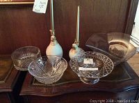Front view of the lot showing clear glass cake dish, two partridge candlestick holders, and large square bowl excluded from sale.