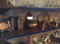Bookshelf with various decor including books, brass container, picture frame, mirror, plates, and figurines.