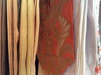 Photo showing several hanging linens including a red and beige floral/paisley cloth with a pointed edge, and adjacent cream/white and tan fabrics.