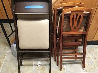 Stack of five folding chairs including three metal framed chairs with beige cushions and two wooden framed chairs with decorative backs.