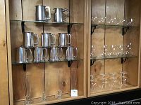 Pewter steins arranged on two glass shelves, nine in total, with two additional similar pewter pieces above