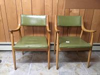 Front view of two mid-century modern blonde wood chairs with green oil cloth seats and backs, showing overall design and condition.