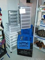 Wide shot of plastic storage drawer units and milk crates stacked together showing multiple drawer sizes and colors.