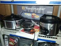 Two crock pots, boxed Toastmaster appliance, foil pans underneath on white wire shelving