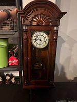 Full view of wooden Howard Miller wall clock showing arched top, glass door, and pendulum