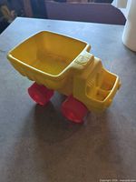 Left side view of yellow plastic Playskool dump truck with red wheels