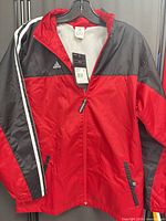Front view of Adidas youth red and black full-zip shell jacket on hanger showing logo, stripes and overall condition