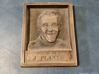 Front view of rectangular sculptured plaque showing J. Plante portrait and name
