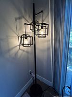Full view of floor lamp standing in corner, round base, three cage shades illuminated