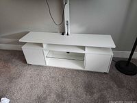 Front view of white TV stand showing side cabinets, centre glass shelf, LED cord and TV mount pole