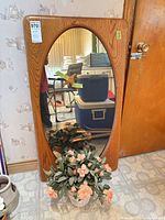 Full view of mirror leaning against wall with floral arrangement in front