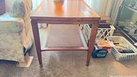 Front view of mid-century wood side table with cane shelf and metal-capped legs