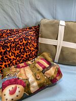 Group shot showing flame pillows, khaki pillow with ribbon, and folded snowman blanket