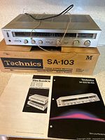 Front view of Technics SA-103 receiver atop original box with both manuals shown