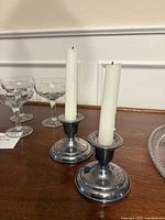 two silver-plated candlesticks with candles on wood surface