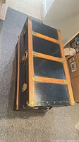 Trunk on side showing top, wood slats, brass corners