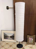 Full view of floor lamp with two framed prints leaning at base