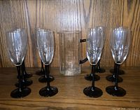 Full set of 12 champagne flutes with black stems and matching clear glass pitcher displayed on shelf