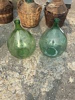 Two green glass demijohn bottles on ground