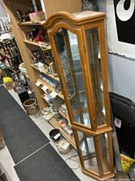 Full view of tall corner curio cabinet showing wooden frame, glass panels, and mirrored back