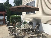 Wide view of the full patio set including six chairs, round glass table, umbrella and stand in an outdoor patio setting.