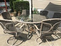 Outdoor patio table surrounded by six beige cast aluminum swivel chairs with mesh fabric seats and backs. Patio set shown on concrete deck.