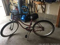 Full side view of pink cruiser bicycle with step-through frame, single gear, wide seat, and black handlebars in garage.