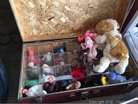 Open red steamer trunk with clear compartments holding various Beanie Babies plush toys, visible brand tags