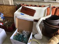 Overall view showing the plastic serving cart, cardboard box with Ball mason jars inside, and nearby flower pots.