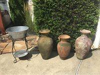 Photo of three decorative outdoor urns placed next to an aluminum ice stand outside on concrete with greenery in background.
