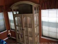 Full view of the distressed green wooden hutch showing curved top, glass-panel sides and double front doors, with bottom drawer closed.