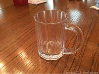 Clear Tiffany & Co. crystal bar mug on wood table, facing front to show handle and facets.