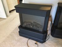 Front view of Dimplex black electric air heater showing faux fireplace logs and power cord.